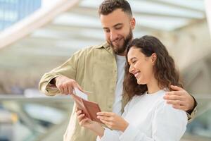 Cheerful couple looking at travel documents while waiting in bright airport terminal photo