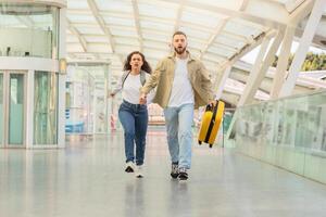 determinado Pareja corriendo mediante aeropuerto corredor con maleta, molesto a captura vuelo foto