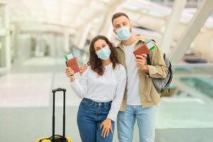 contento Pareja en médico mascaras posando en aeropuerto con pasaportes y Entradas foto