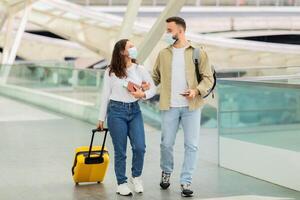 Young Couple In Medical Masks Walking With Suitcase At Airport Hallway photo