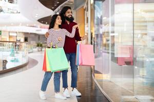 Happy young indian couple have shopping together, checking shop windows photo