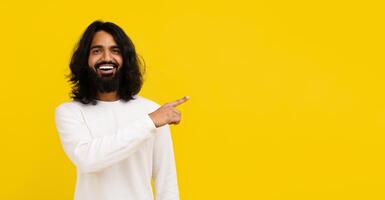Cheerful young indian man pointing at copy space photo