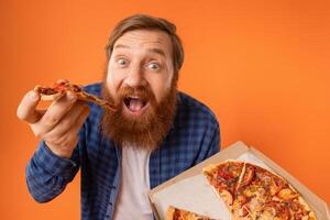 gracioso hombre con rojo pelo y barba comiendo pizza, estudio foto