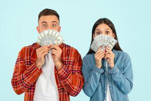 Surprised young man and woman holding dollar money cash, studio photo