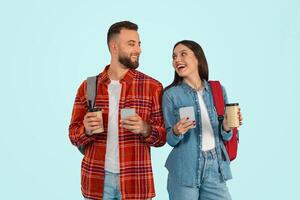 students couple holding phones with backpacks and takeaway coffee, studio photo