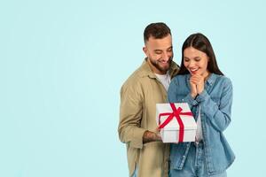 young woman receiving wrapped gift box from husband, blue backdrop photo