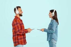 Couple With Headphones Holding Smartphones Listening Music Against Blue Background photo