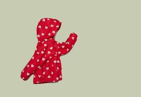 Child's raincoat red color with white heart. Baby girl outwear on blue background photo