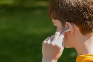 cerca arriba de adolescente chico utilizando auriculares exterior. estilo de vida chico vistiendo inalámbrico auriculares, escuchando canción o audio libro en teléfono inteligente, Copiar espacio. foto