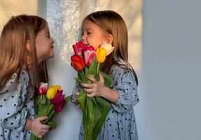 retrato de dos sonriente pequeño niña con un ramo de flores de tulipanes estilo de vida, De las mujeres o de la madre día. hermanos o gemelo día. espacio para texto. foto