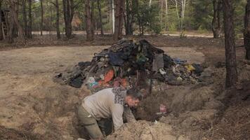 un trabajador borra el bosque de escombros, lanza basura fuera de un agujero sobre un grande pila de basura. seguro ecología concepto. video