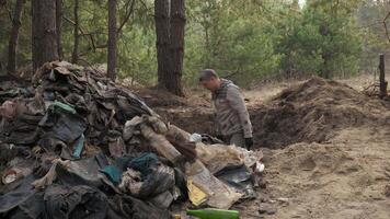 A worker clears the forest of debris, throws garbage out of a hole onto a large pile of garbage. Safe ecology concept. video