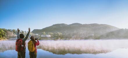 An Asian couple who is standing and watching the fog rising on the lake in the morning. Travel Ban Rak Thai village, Mae Hong Son in Thailand. Take a picture of the lake photo