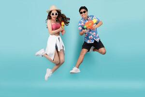 Happy Asian couple jumping and using water guns on blue background. Songkran Festival in Thailand photo