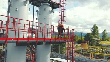 Aerial view gas station operator climbs to the top of the station. Modern gas complex in the mountains. A gas worker climbs the ladder of the gas distribution unit against the backdrop of mountainous video