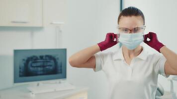 porträtt av en läkare bär en skyddande mask på en dental klinik innan kirurgi. ung tandläkare läkare. video