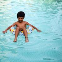 Happy Indian boy swimming in a pool, Kid wearing swimming costume along with air tube during hot summer vacations, Children boy in big swimming pool. photo