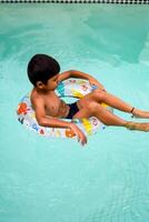 contento indio chico nadando en un piscina, niño vistiendo nadando disfraz a lo largo con aire tubo durante caliente verano vacaciones, niños chico en grande nadando piscina. foto