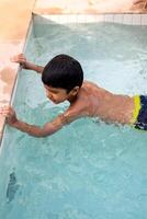 contento indio chico nadando en un piscina, niño vistiendo nadando disfraz a lo largo con aire tubo durante caliente verano vacaciones, niños chico en grande nadando piscina. foto