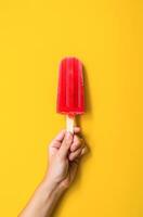 ai generado mano participación un vibrante rojo paleta de hielo en contra un brillante amarillo antecedentes foto