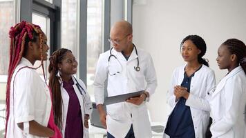 ein Mannschaft von afrikanisch amerikanisch Ärzte, einschließlich 4 Frauen und 1 Mann, haben ein Geschäft Konversation während Stehen im ein Klinik video
