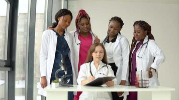 Young doctors of different races have a discussion standing at a table while one of them makes notes video