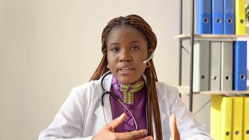 Jeune africain américain femme médecin ayant bavarder ou consultation sur portable à la recherche directement à le caméra video