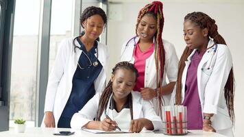 Young doctors have a discussion standing at a table while one of them makes notes video