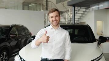 retrato de un joven hombre cerca un nuevo eléctrico coche en un coche concesión video