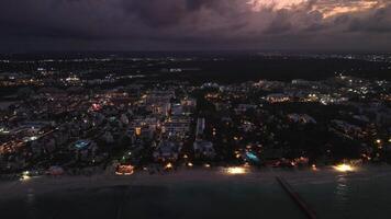 escénico aéreo ver desde zumbido de turístico costero ciudad en contra un espectacular púrpura puesta de sol cielo, iluminado por vibrante ciudad luces. vuelo adelante video