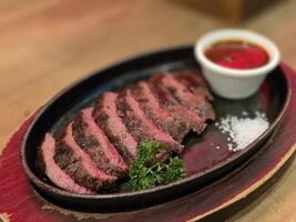 Grilled Juicy steak medium rare beef with herbs and spices on pan hot served with salt and brown sauce on wooden table. photo