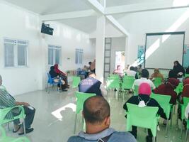 elderly people are sitting on green chairs queuing for health checks at the community health center. regular elderly health checks at semarang march 12 2024 photo