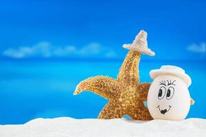 White egg with smile hugs starfish on sea . Easter in hot countries. Copy space photo