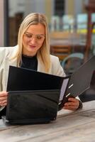 a business woman sits in front of a cafe and reads a file folder photo