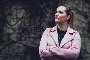 woman in a pink jacket is standing in front of a wall photo