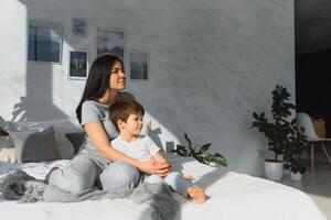 Young mother with her 5 years old little son dressed in pajamas are relaxing and playing in the bed at the weekend together, lazy morning, warm and cozy scene. Family home shoot. photo