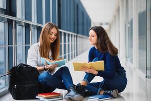 two pretty female students with books sitting on the floor in the university hallway photo