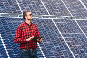 Young engineer with tablet computer standing near solar panels outdoors photo