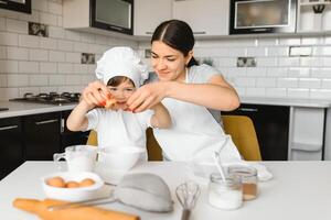 contento madre y su pequeño hijo sacudida crudo huevos en cuenco antes de haciendo masa para hecho en casa Pastelería en el cocina foto