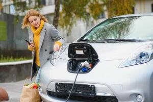 Woman with phone near an rental electric car. Vehicle charged at the charging station photo