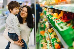 mujer y niño chico durante familia compras con carretilla a supermercado foto