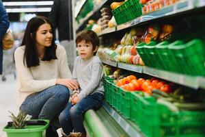 joven madre con su pequeño bebé chico a el supermercado. sano comiendo concepto foto