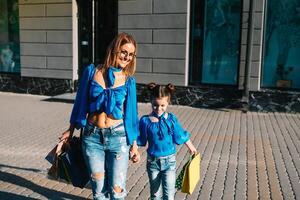 venta, consumismo y personas concepto - contento joven mujer su hija con compras pantalones caminando ciudad calle foto