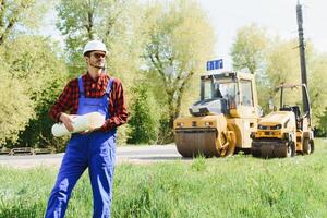 engineer near road machinery. The concept of building a new asphalt road. Road repair. Road service worker near the rink. photo