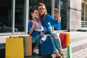 Young mother and her daughter doing shopping together. woman with girl child after shopping in street. woman with daughter with shopping bags outdoors. Woman and her daughter after shopping photo