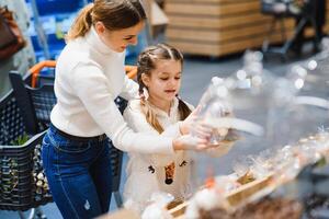 Family in the supermarket. Beautiful young mom and her little daughter smiling and buying food. The concept of healthy eating. Harvest photo