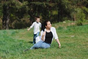 contento joven madre es jugando con su bebé en un parque en un verde césped. felicidad y armonía de familia vida. genial familia vacaciones. bueno fin de semana. madres día. día festivo. el concepto de un contento familia foto