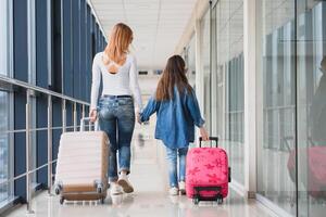 Happy young mother and her daughter walking in the airport terminal while carrying a suitcase. High season and vacation concept. Relax and lifestyles photo