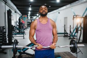 Concentrated African-American sportsman training bicep with heavy barbell in gym photo