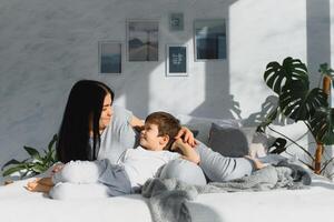 Mother playing with her little cute son in the morning in bedroom. Happy family time. photo